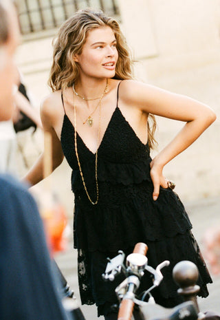 A woman wearing a black lace tiered spaghetti-strap dress and gold necklaces